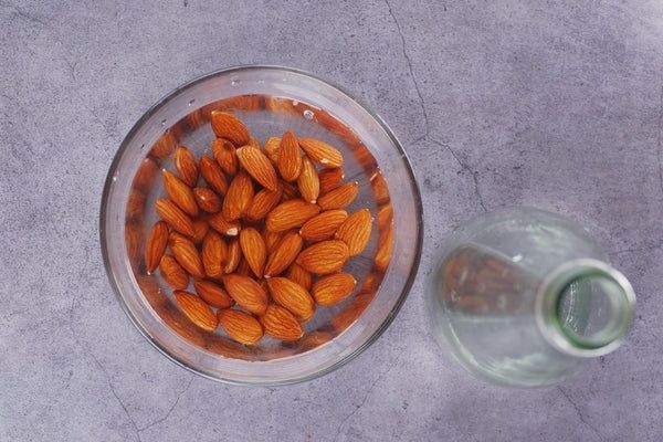 Mandlar blötläggs i en skål med vatten bredvid en glasflaska