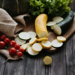 Råa zucchini, gul squash, tomater och sallad på skärbräda