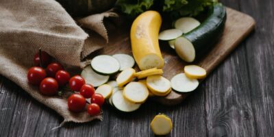 Råa zucchini, gul squash, tomater och sallad på skärbräda