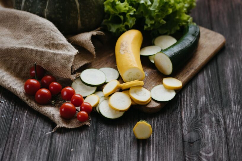 Råa zucchini, gul squash, tomater och sallad på skärbräda